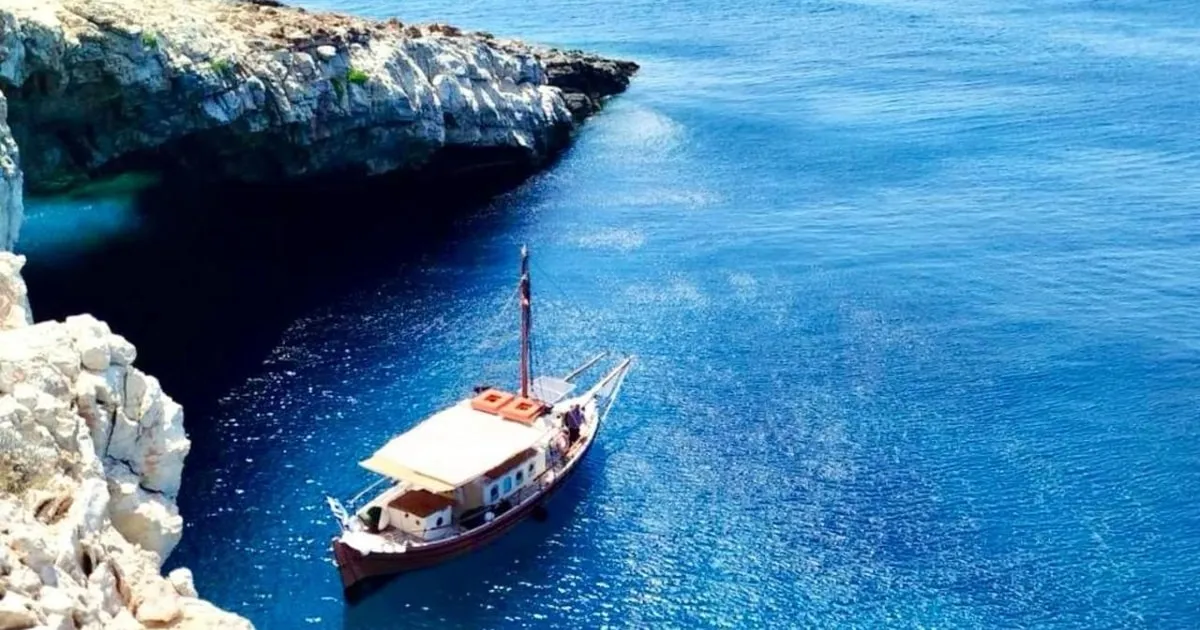 Dramatic limestone cave cliffs over clear water at the Pirate Cave near Antiparos on a half-day boat trip from Paros
